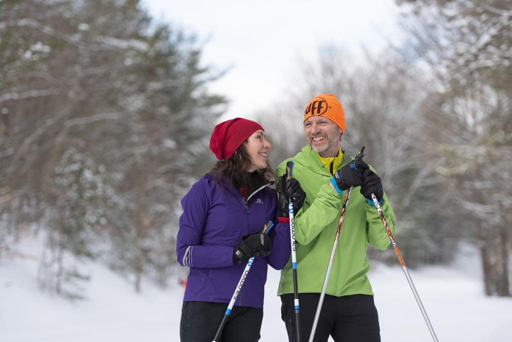 Cross country skiing couple smiling and laughing with ski poles in hand on a wintery day