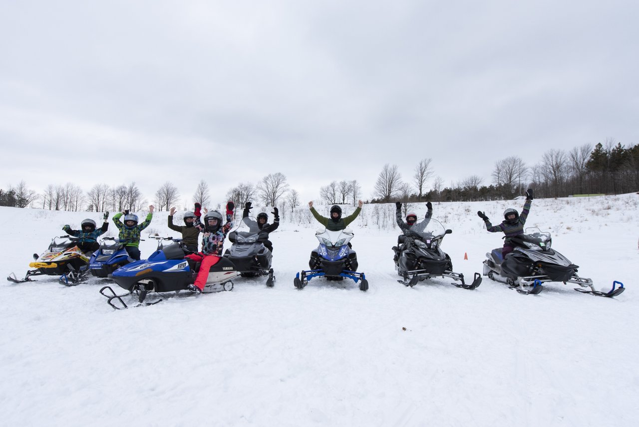 SMART Adventures group of people all on snowmobiles lined up with their arms up in the air cheering